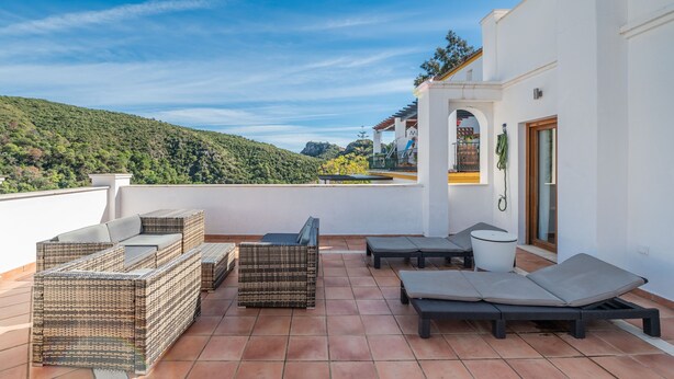 A terrace with wicker furniture, a small table, and a door with a towel hanging. - Apartment '3 Bed  in Benahavis' with Mountain View, Wi-Fi and Air Conditioning (Benahavís)