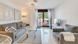 A modern living room with a sofa, armchair, glass coffee table, and a TV on a stand. - Apartment '3 Bed  in Benahavis' with Mountain View, Wi-Fi and Air Conditioning (Benahavís)