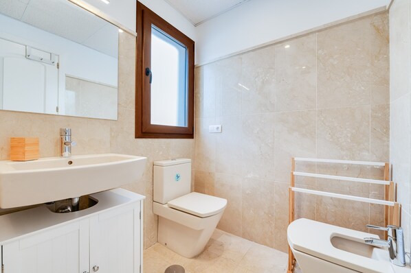 A bathroom with a toilet, sink, mirror, and a window.