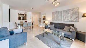 A modern living room with a grey sofa, a glass coffee table, and a dining area with chairs and a table. - Apartment '3 Bed  in Benahavis' with Mountain View, Wi-Fi and Air Conditioning (Benahavís)