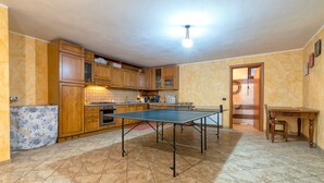A kitchen with a ping pong table, wooden cabinets, and a tiled floor.