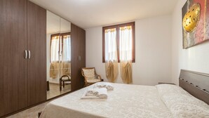 A bedroom with a large bed, a wardrobe, a chair, and a window with curtains.