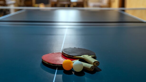 A ping pong table with two paddles and two balls.