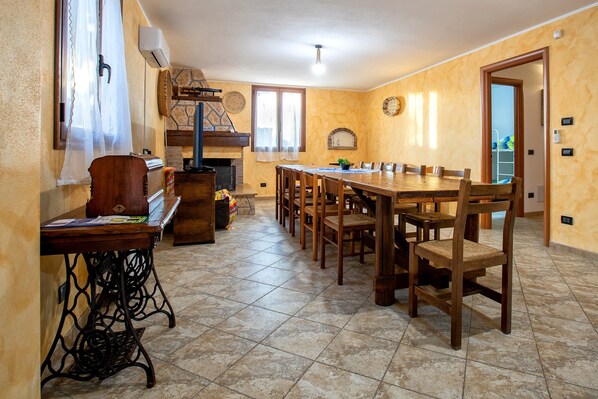 A dining area with a long wooden table and chairs, a sewing machine, and a fireplace.