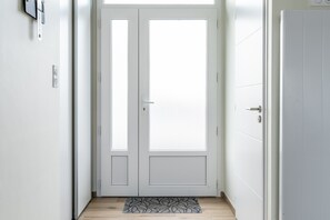 Eine weiße Tür mit einer satinierten Glasscheibe, eine Fußmatte und ein an der Wand befestigter Lichtschalter.