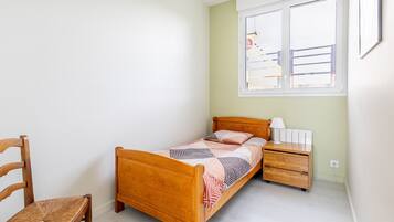 A bedroom with a wooden bed, a nightstand, a chair, and a window with a view of a balcony.
