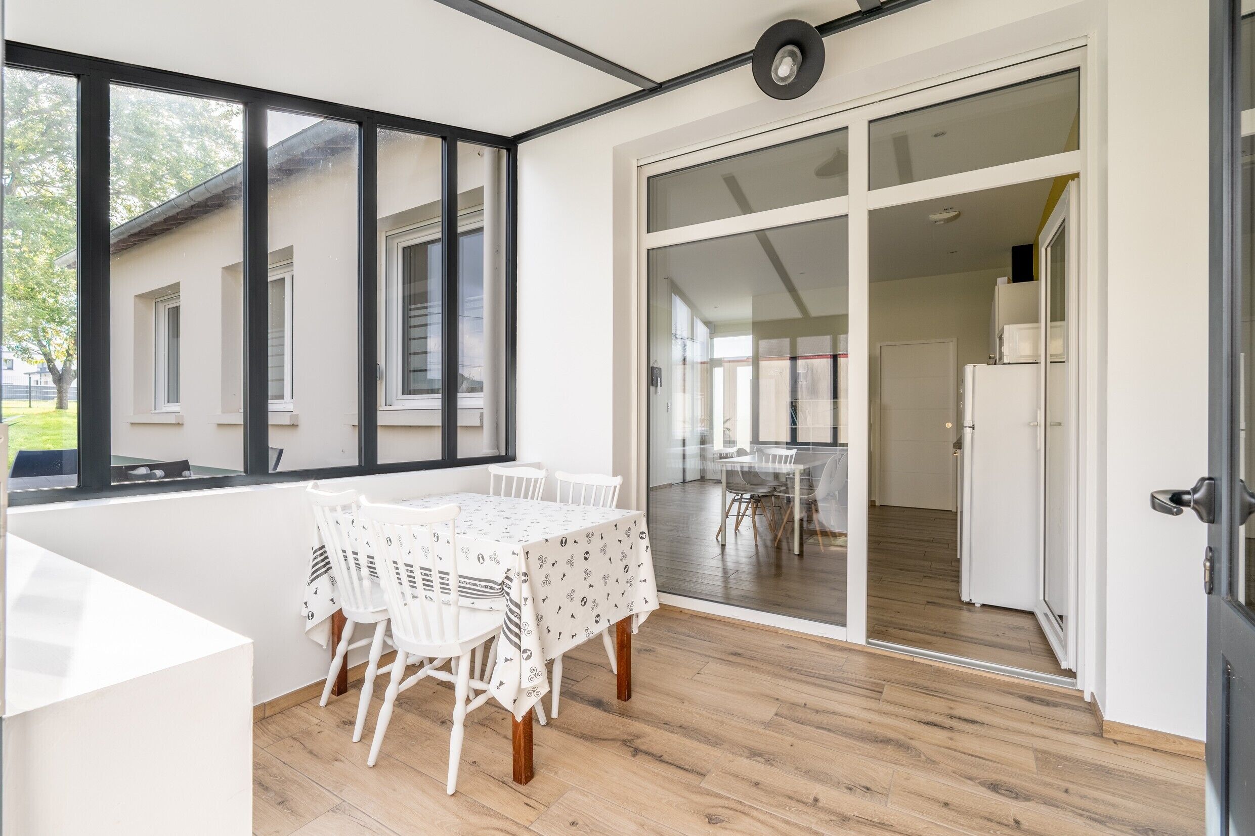 A modern room with a large window, a dining table with chairs, and a sliding glass door leading to another room.