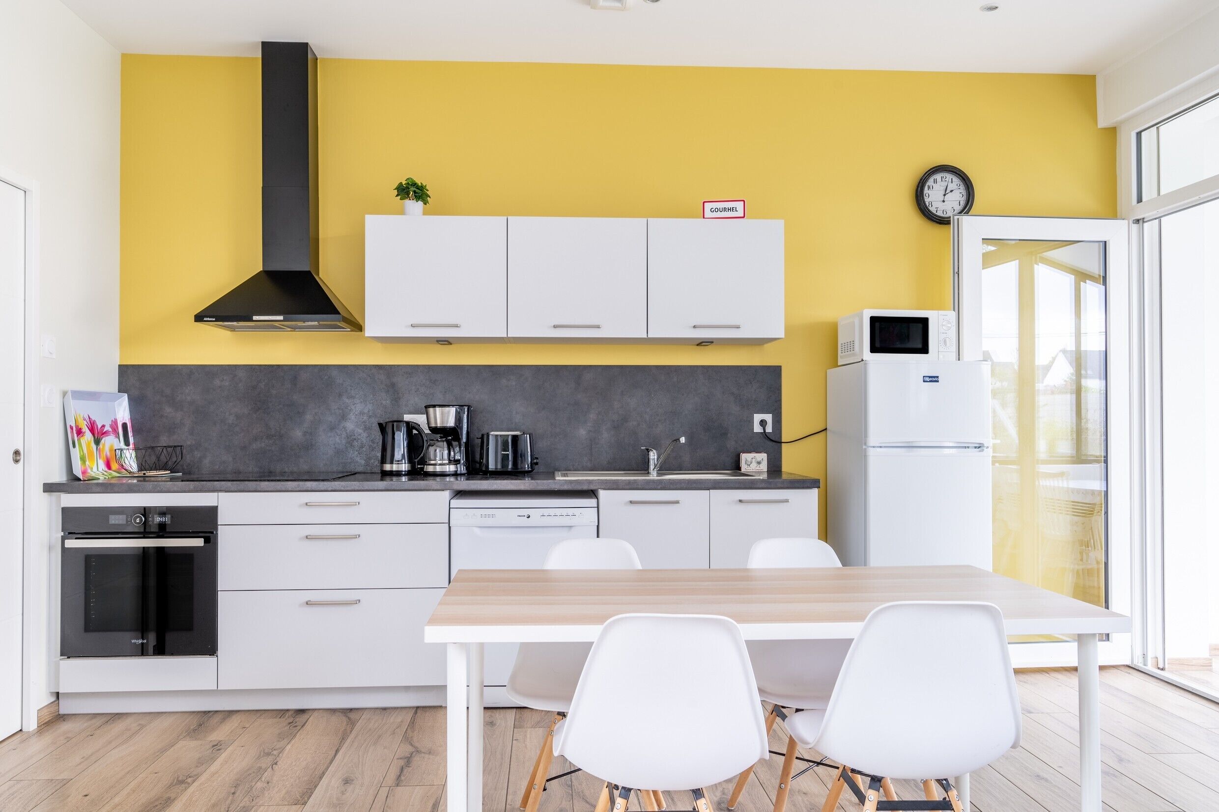 Une cuisine moderne avec des armoires blanches, une hotte noire, un four à micro-ondes et une horloge murale.