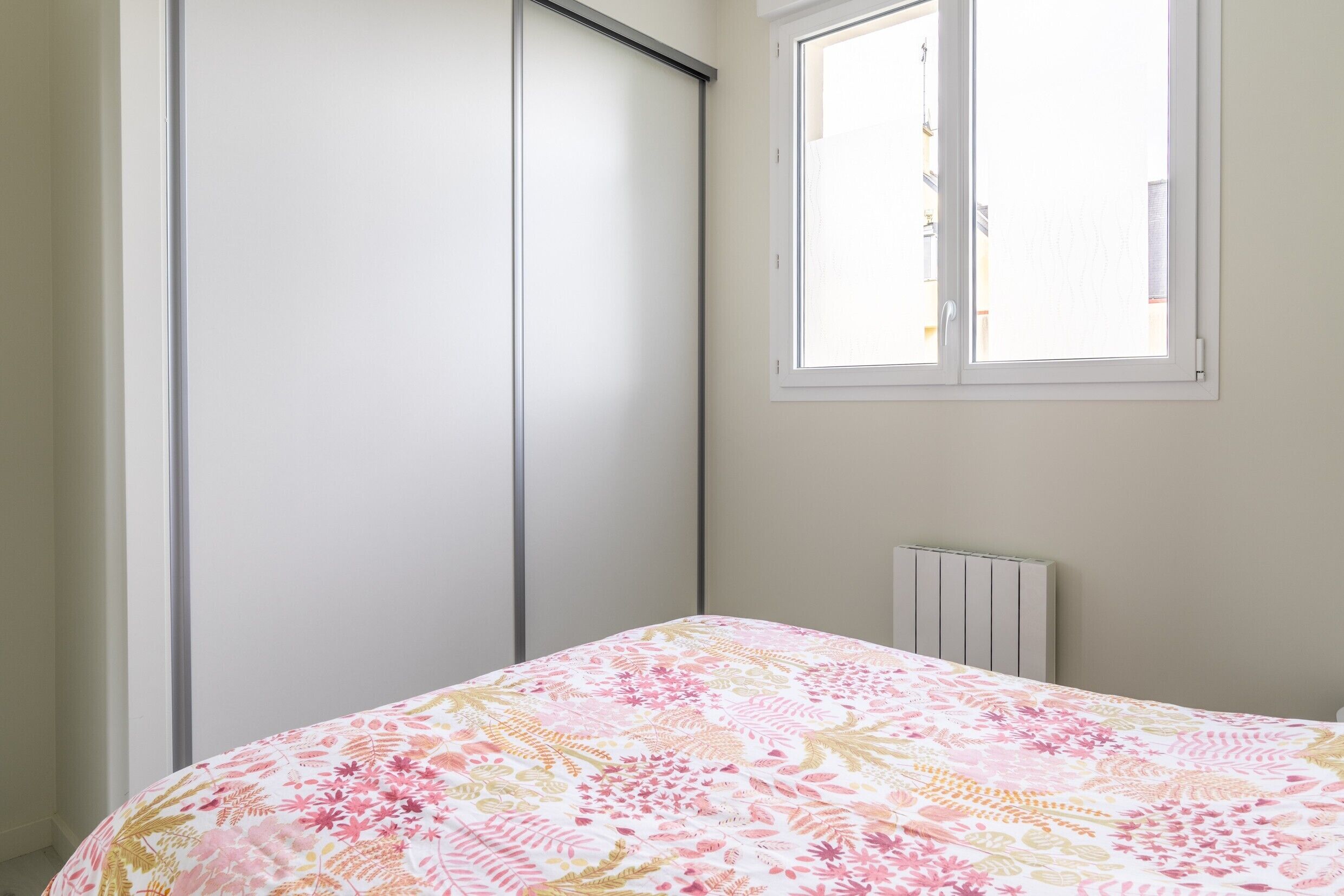 A bedroom with a bed, a window, a radiator, and a wardrobe.