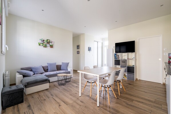 Un salon moderne comprenant un canapé, un pouf, une table à manger, des chaises et un téléviseur.