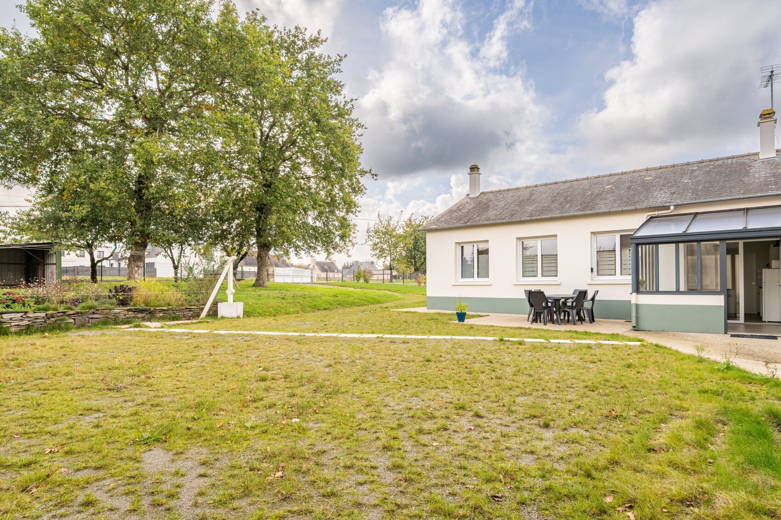 Een huis met een overdekt terras, een gazon en een grote boom.