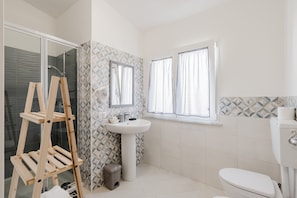 Ein Badezimmer mit Duschkabine aus Glas, einer Holzleiter, einem Waschbecken auf Säule und einer Toilette.