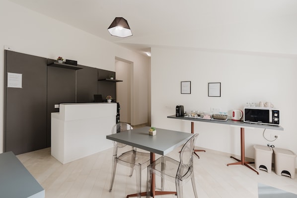 Eine moderne Küche mit Essbereich, transparenten Stühlen, einem grauen Tisch, einer Hängeleuchte und einer Mikrowelle auf einer Arbeitsplatte.