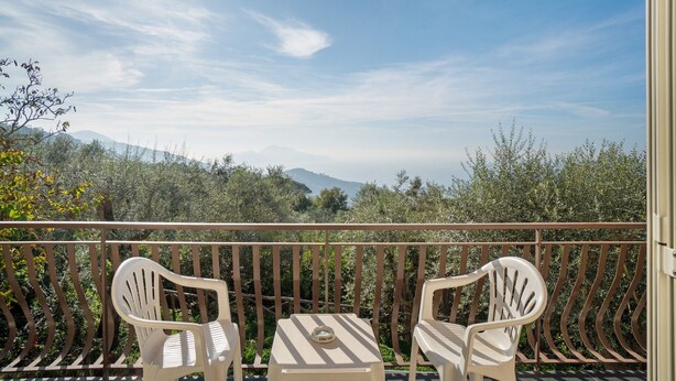 A balcony with two white plastic chairs and a small table, overlooking a mountainous landscape.