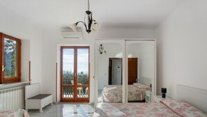 A bedroom with a bed, a desk, a chair, a wardrobe, and a balcony.