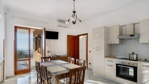 A modern kitchen with a dining area, a TV mounted on the wall, and a balcony with a view.