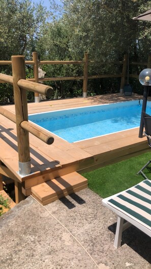 A swimming pool with a wooden deck, a lounge chair, and a pergola structure.
