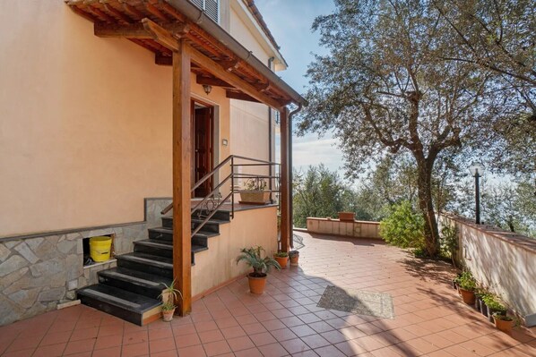 A building with a stone facade, a wooden staircase, and a tiled patio with potted plants.