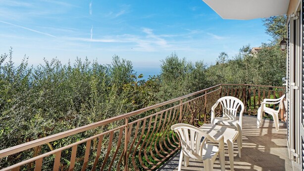 A balcony with a railing, a table with chairs, and a view of trees and buildings.
