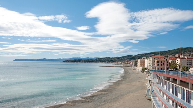 Un hôtel situé sur la côte, avec vue sur la plage, une promenade et un paysage vallonné en arrière-plan.