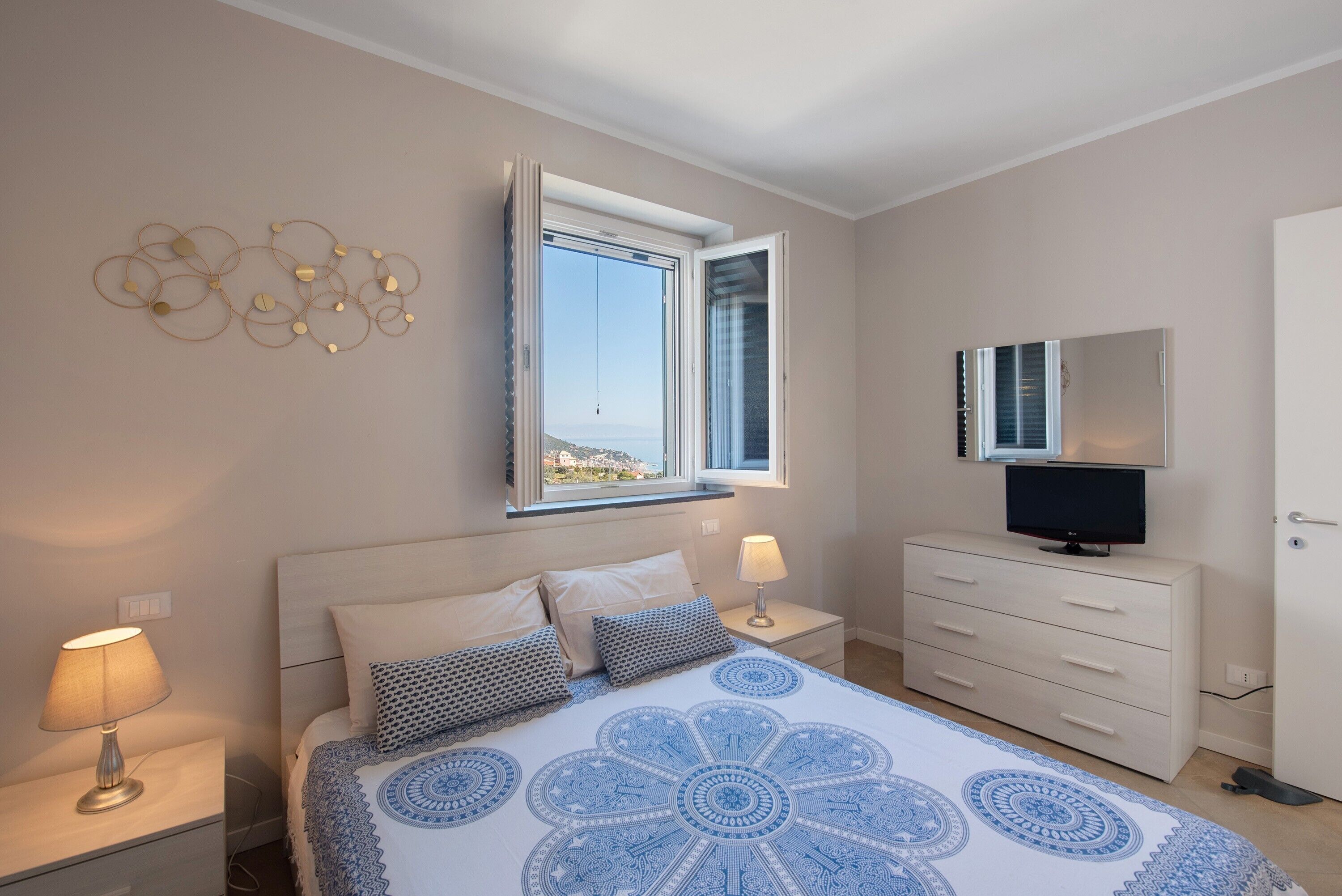 Une chambre à coucher comprenant un lit, une table de chevet, une commode, un téléviseur et une fenêtre donnant sur un paysage dégagé.