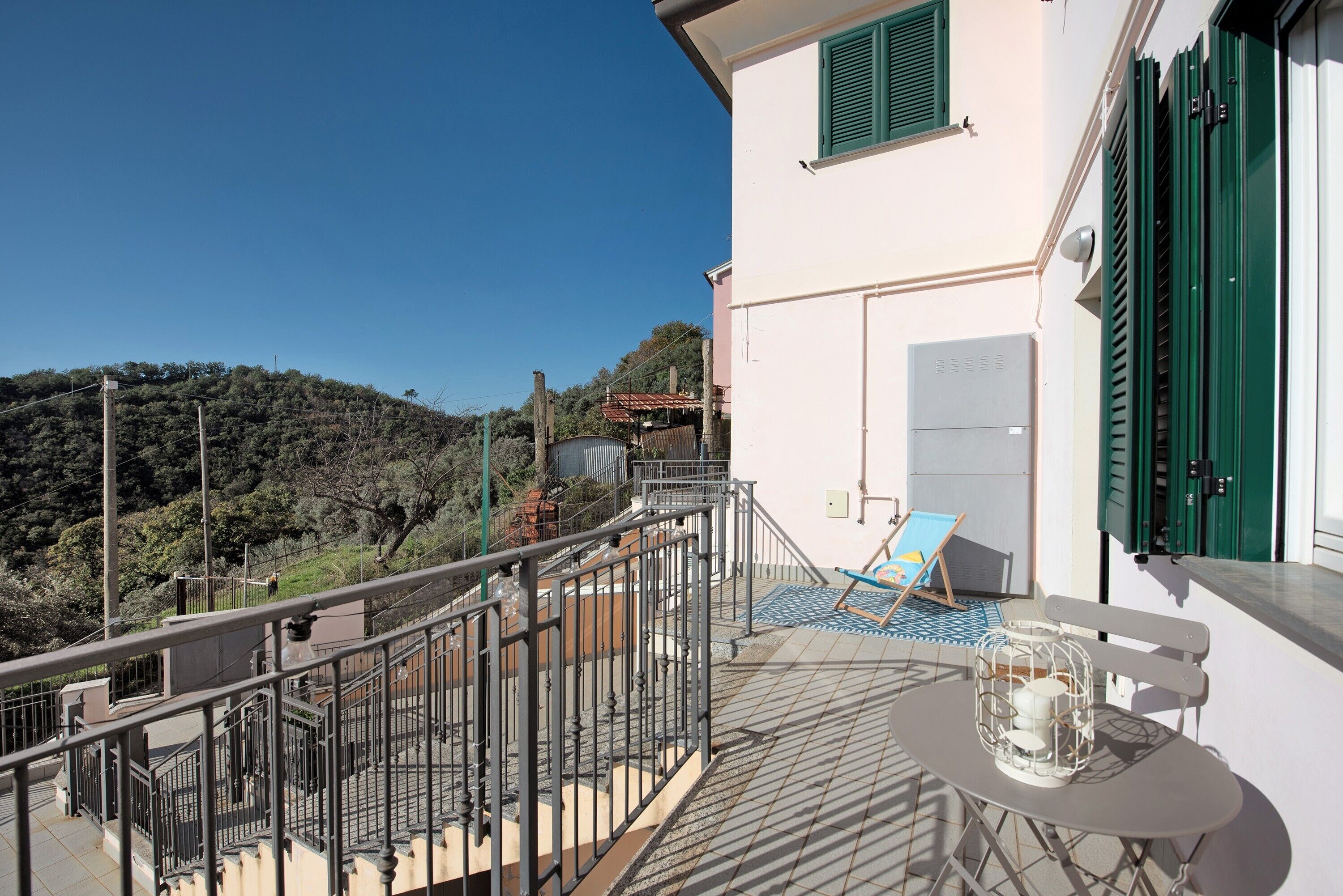 A balcony with a table, chairs, and a view of a hillside.