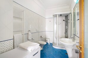 Un baño con inodoro, lavabo, ducha y perchero para toallas.