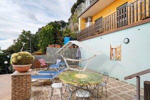 Une terrasse avec une table ronde, des chaises, un cactus en pot et un fauteuil de jardin bleu.
