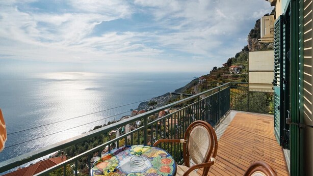 A balcony with a view of the sea, a table with a colorful tablecloth, and a chair. - Amalfi Room with Sea View (Furore)
