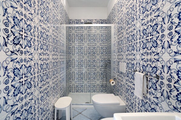 A bathroom with blue floral tiles, a toilet, a sink, and a shower area.