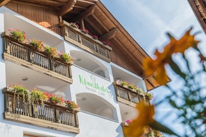 Un edificio con balcones decorados con flores, un letrero que dice 'Klawsthaler Pension Café' y detalles arquitectónicos de madera.