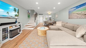 Un salón espacioso con un televisor de pantalla plana grande, un sofá color beige y una escalera que lleva a una cocina.