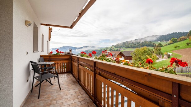 En balkon med gelænder i træ, et bord og stole.