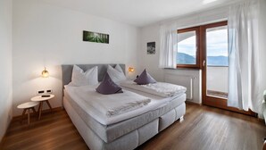 A bedroom with a bed, bedside tables, a window with curtains, and a view of the outdoors.