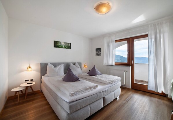 A bedroom with a bed, bedside tables, a window with curtains, and a view of the outdoors.