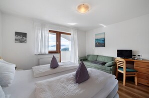 A hotel room with two beds, a green sofa, a wooden desk, and a television.