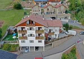 Un immeuble à plusieurs étages doté de balcons, d’un espace extérieur couvert aménagé en coin salon et d’un parking.