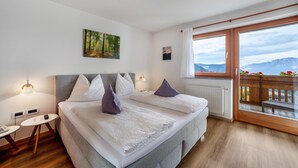 Een slaapkamer met een bed, nachtkastjes, een raam met uitzicht en een balkon met bloemen.