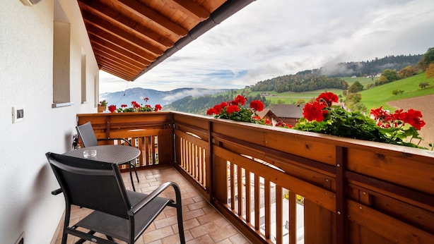 Un balcon avec une balustrade en bois, une table avec une chaise et des fleurs rouges.