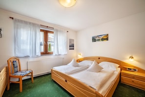 Une chambre à coucher avec un lit en bois, une chaise, une fenêtre avec des rideaux, un radiateur et des lampes fixées au mur.