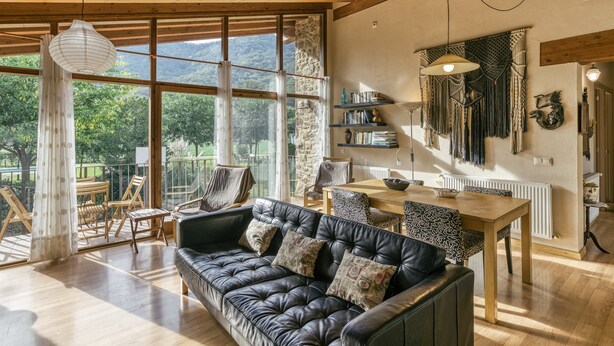 Amplia sala de estar con sofá de cuero, mesa de comedor de madera y grandes ventanales con vistas a la montaña.
