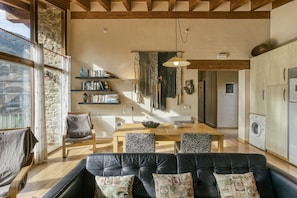 A spacious living area with a wooden dining table, black leather sofa, and a stone wall.