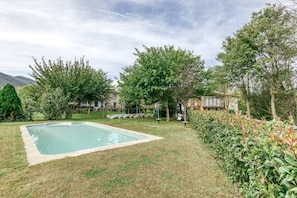 A swimming pool surrounded by grass and trees, with a building in the background.
