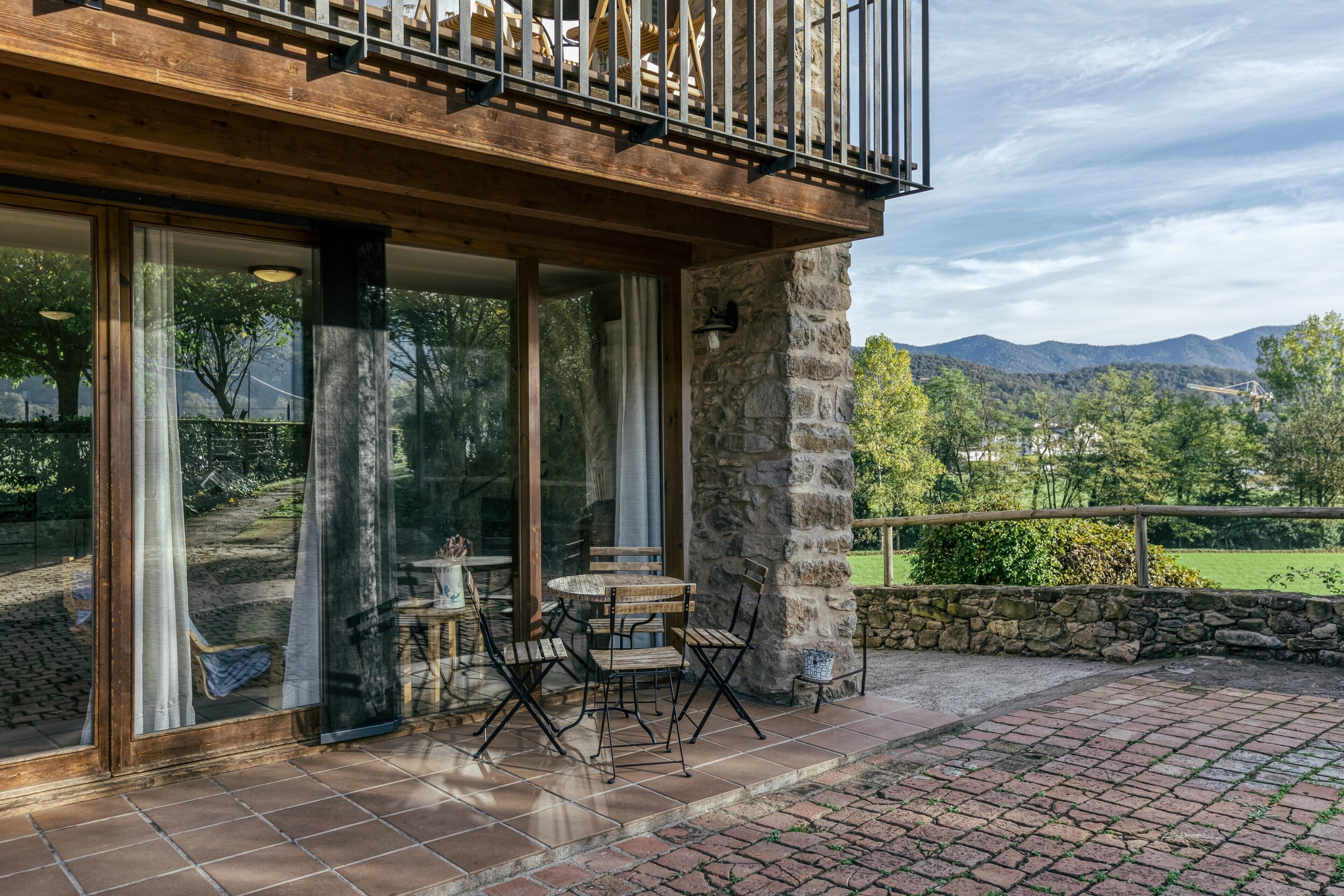 Un patio con una mesa y sillas, un muro de piedra y vistas a montañas.