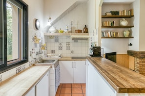 A kitchen with white cabinets, a wooden countertop, a window, and a bookshelf with books and decorative items.