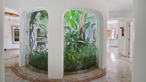 A hallway with a glass enclosure featuring tropical plants, a framed picture on the wall, and a fire extinguisher. - Holiday Home 'Casa Isabella' with Private Pool, Wi-Fi and Air Conditioning (Vilamoura)