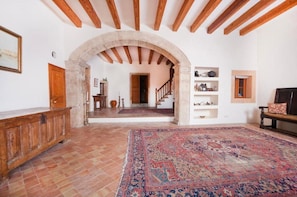 Un intérieur agrémenté d’un grand tapis, de poutres en bois, d’une arche en pierre et d’un escalier menant à une autre pièce.