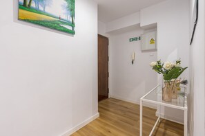 A hallway with a painting, a fire exit sign, a warning sign, and a table with flowers. - Apartment 'Granada Garaje Gratis' with Wi-Fi and Air Conditioning (Urbanización los Vergeles)