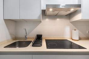Una cucina moderna con lavello in acciaio inossidabile, piano cottura a induzione nero e cappa aspirante.