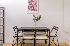 Zona pranzo con tavolo, quattro sedie, un vaso con piante e un quadro appeso al muro.